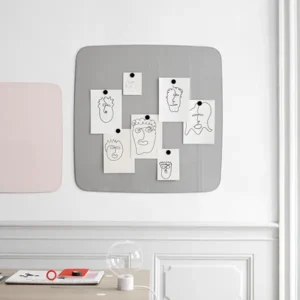Graue Lintex Flow Magnettafel mit abgerundeten Ecken und angehefteten Zeichnungen in einem hellen, minimalistischen Raum.