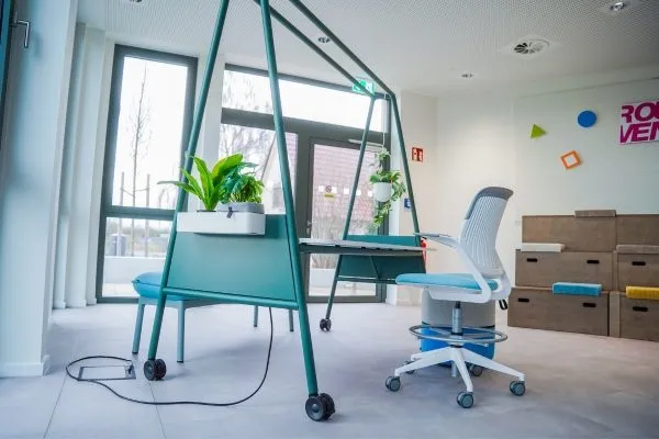 Höhenverstellbarer Stehschreibtisch mit Pflanze und Bürostuhl, im Hintergrund Umzugskartons