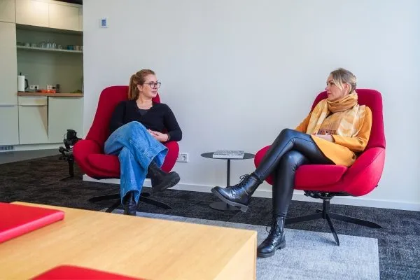 Zwei Frauen sitzen in roten Sesseln und unterhalten sich in einem Büroraum mit Holzboden