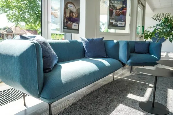 Petrolfarbenes Sofa mit Kissen in einem hellen Wartebereich vor großen Fenstern