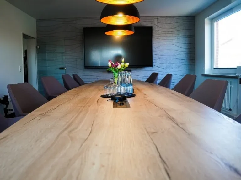 Konferenzraum mit langem Holztisch, orangen Pendelleuchten und Bildschirm an der Wand